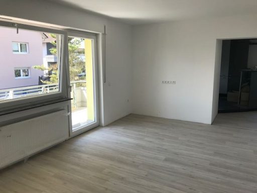 Heller Raum mit Fenster und Balkon, helle Wände, niedrigem Bodenbelag und leerer Fläche.