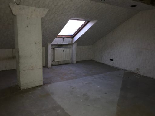 Leere Dachgeschoss-Raum mit einer Dachfenster und betonierten Wänden.