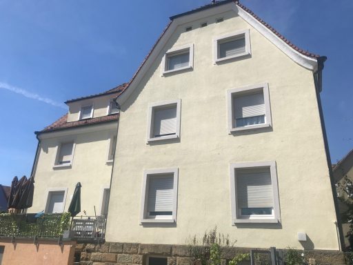 Helles, dreigeschossiges Wohnhaus mit mehreren Fenstern und einem Spitzdach.