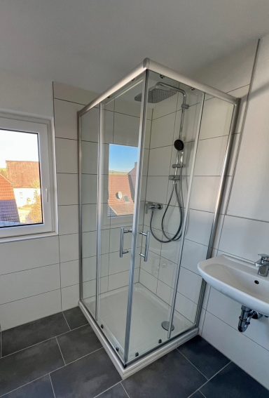 Moderne Dusche mit Glaswänden, Handbrause und schlichten Fliesen.