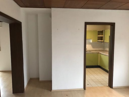 Heller Raum mit einem offenen Durchgang zur grünen Küche und Holzdecke.