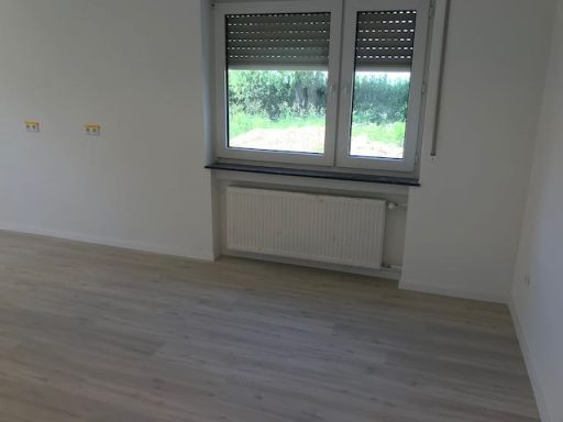Helle, leere Raum mit Fenster, Heizung und Laminateboden. Blick ins Grüne.