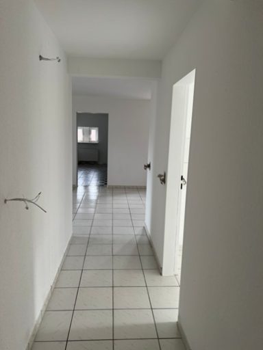 Langer, heller Flur mit grauer Wand und zwei Türen. Fliesenboden in neutralen Farben.
