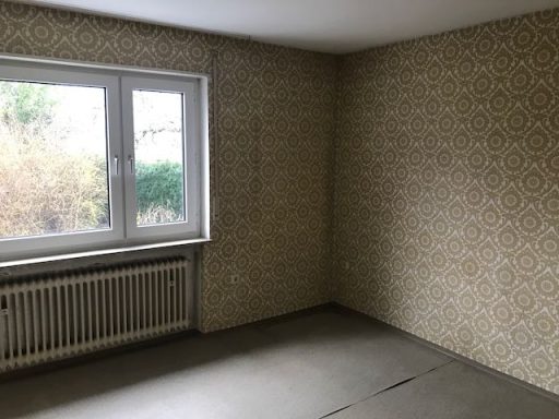 Leerer Raum mit Fenster, tapetenverziert und einem Heizkörper an der Wand.