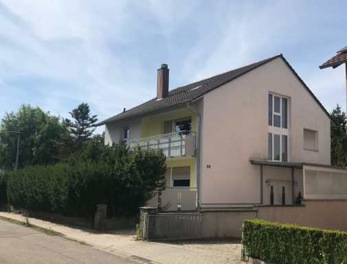 Helles Wohnhaus mit grüner Hecke und blauem Himmel im Hintergrund.