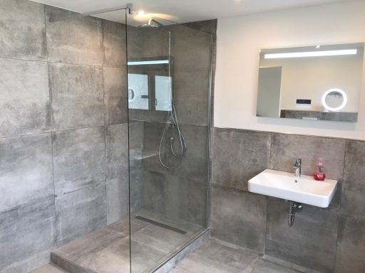 Moderne Badezimmeransicht mit gläserner Dusche und Waschbecken. Wände in Grautönen.