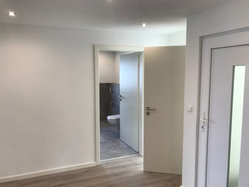 Heller Raum mit offener Tür zu einem Badezimmer, modern und schlicht eingerichtet.