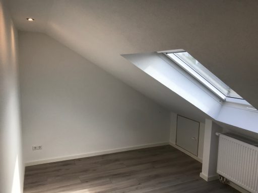 Heller Dachraum mit schrägen Wänden, Dachfenster und Holzfußboden.